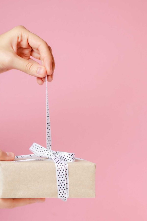 woman hands untie bow on gift box on pink background